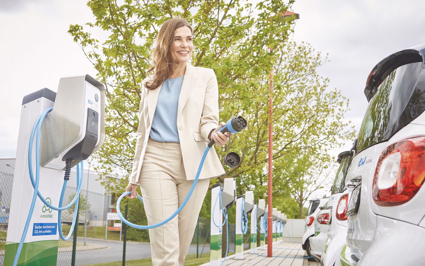 E-Mobilität - Kundin vor Ladestation mit Stecker in der Hand &middot; Hornetz